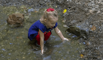 Taryn (4 years old) kneeling down in a creek and feelings the water.