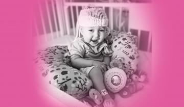 Owen sitting up smiling in crib at the hospital with neonatal baby monitor on his head