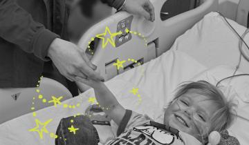 Nurse holding Zach's hand (age) as he's smiling in a hospital bed