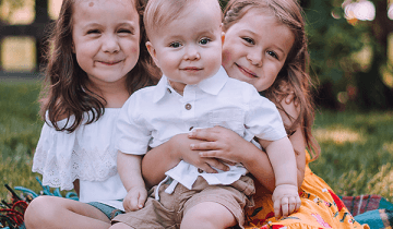Three siblings sitting on a rug with Owen (Age 1) who has CP sitting in the middle