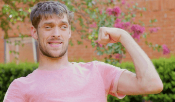 Zach Anner outside in salmon shirt, flexing his arm