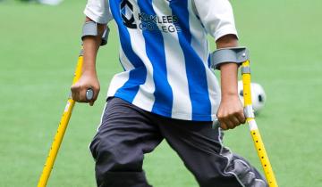 Image of teenage boy using crutches kicking a soccer ball.