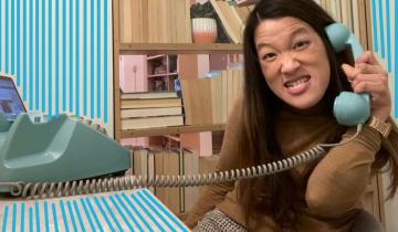 A young woman sits at a desk on the phone smiling. Blue doodles surround her.