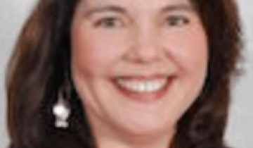 Photo of Mary Ganotti in a red shirt with a black sport coat on a grey background