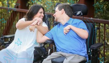 Shelby, a dark haired woman wearing a white dress sitting in a wheelchair next to David who is wear in Blue shirt and khaki pants sitting in his wheelchair.