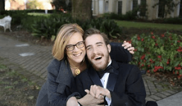 Woman in a grey sweater hugging a man in a tuxedo who is sitting in a wheelchair