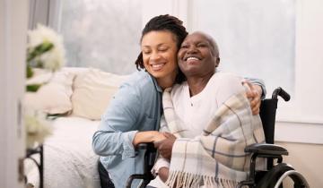 Photo of woman wearing a blue shirt embracing a woman in a wheelchair