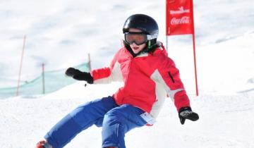 Young person wearing a red and white parka with blue pants and a black helmet snowboarding 