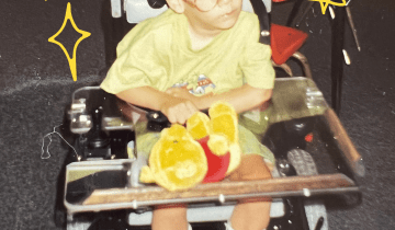 Young David Stoner wearing a yellow shirt and shorts and a pair of glasses in a power wheelchair holding a winnie the pooh teddy bear
