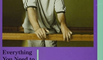 Boy in gray shirt smiling and leaning on a wooden rail