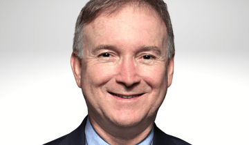 Paulo Selber has short greyish brown hair and is smiling wearing a blue shirt, tie and blue blazer.