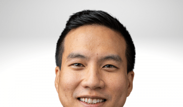 Byron Lai has dark hair and is smiling. He is wearing a white shirt with a dark jacket.