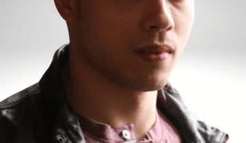Peter has dark brown hair, he is gazing into the camera with a serious expression on his face, wearing a leather jacket