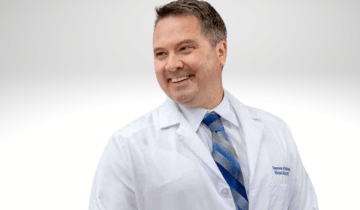 Michael Kruer has short brown hair, he is smiling wearing a lab coat with a blue tie