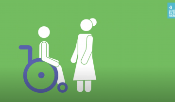 Illustration of a person in a purple wheelchair about to be transferred to standing by a woman standing in front of them. They are drawn on a green background.