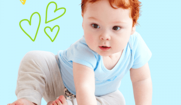 A little baby boy with bright red hair is sitting and playing with a red ball