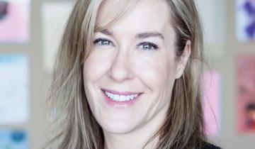 Natalie Maitre has shoulder length sandy blonde hair and blue eyes. She is wearing a blazer and smiling
