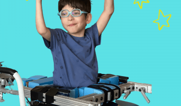 A boy wearing blue shorts and a blue shirt is sitting on a bench with his hands up in the air reaching for stars!