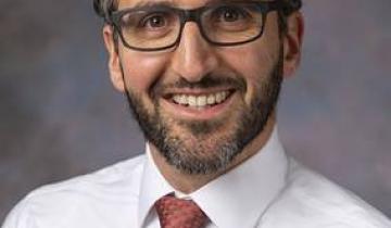 Nathan Rosenberg has dark hair and glasses. He is smiling and wearing a pink shirt with a tie