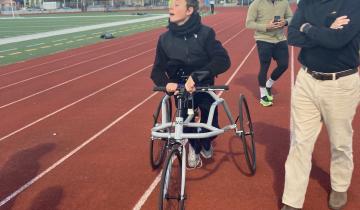 A teenager in a black jacket is using a frame runner to run around a track