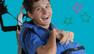 Young man sitting in a wheelchair smiling while wearing a life vest