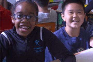 Two students sitting in a classroom at a desk smiling directly at camera
