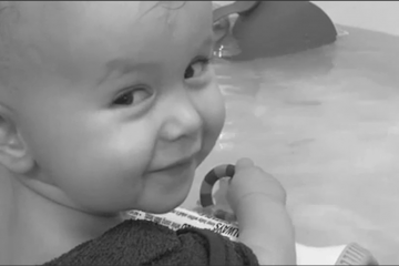 Owen age 1 years old smiling looking behind his shoulder in the bath playing with a toy