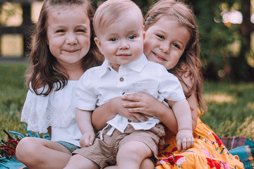 Three siblings sitting on a rug with Owen (Age 1) who has CP sitting in the middle