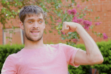 Zach Anner outside in salmon shirt, flexing his arm