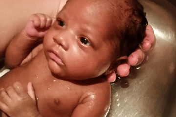 Photo of baby girl being held behind her head while having a bath