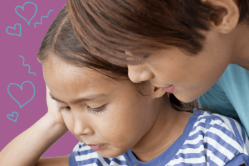 Mother standing over her daughter while they look at something together.