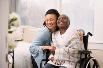 Photo of woman wearing a blue shirt embracing a woman in a wheelchair