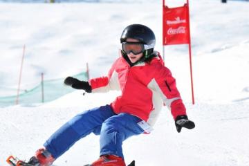 Young person wearing a red and white parka with blue pants and a black helmet snowboarding 