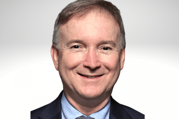 Paulo Selber has short greyish brown hair and is smiling wearing a blue shirt, tie and blue blazer.