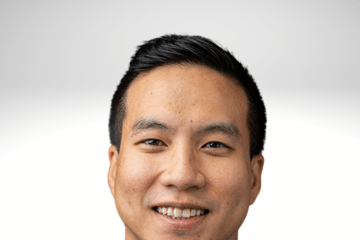 Byron Lai has dark hair and is smiling. He is wearing a white shirt with a dark jacket.
