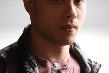 Peter has dark brown hair, he is gazing into the camera with a serious expression on his face, wearing a leather jacket