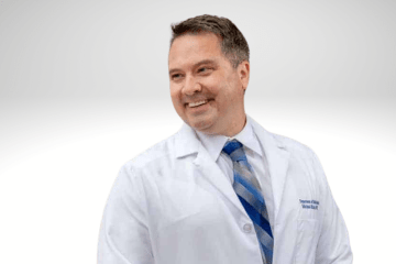 Michael Kruer has short brown hair, he is smiling wearing a lab coat with a blue tie