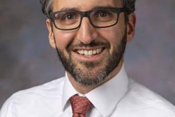 Nathan Rosenberg has dark hair and glasses. He is smiling and wearing a pink shirt with a tie