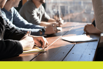 Image of people sitting at a table taking notes with a pencil and paper